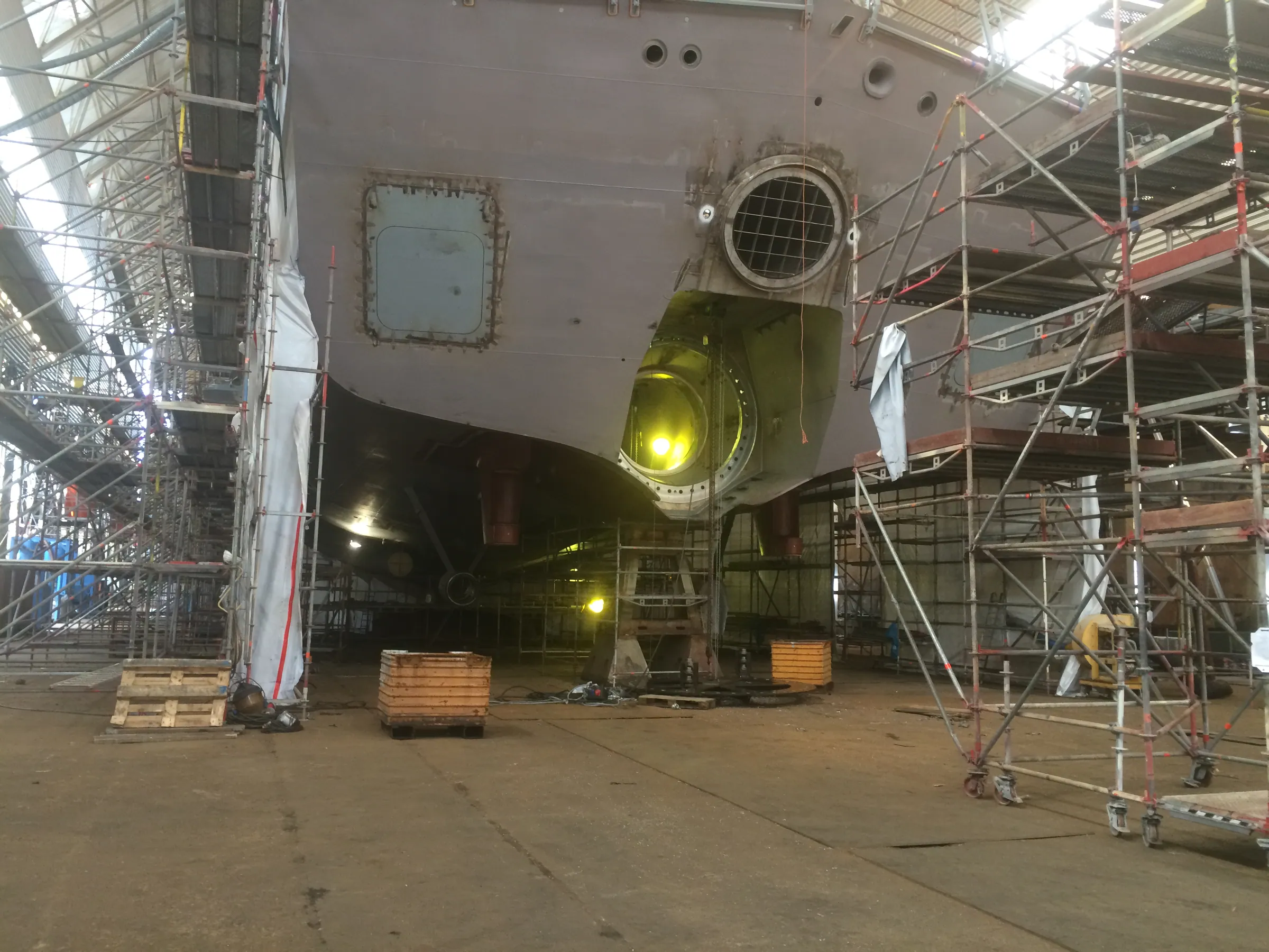 A vessel supported in a covered dry dock, surrounded by scaffolding, with a thruster tunnel opening in the hull.