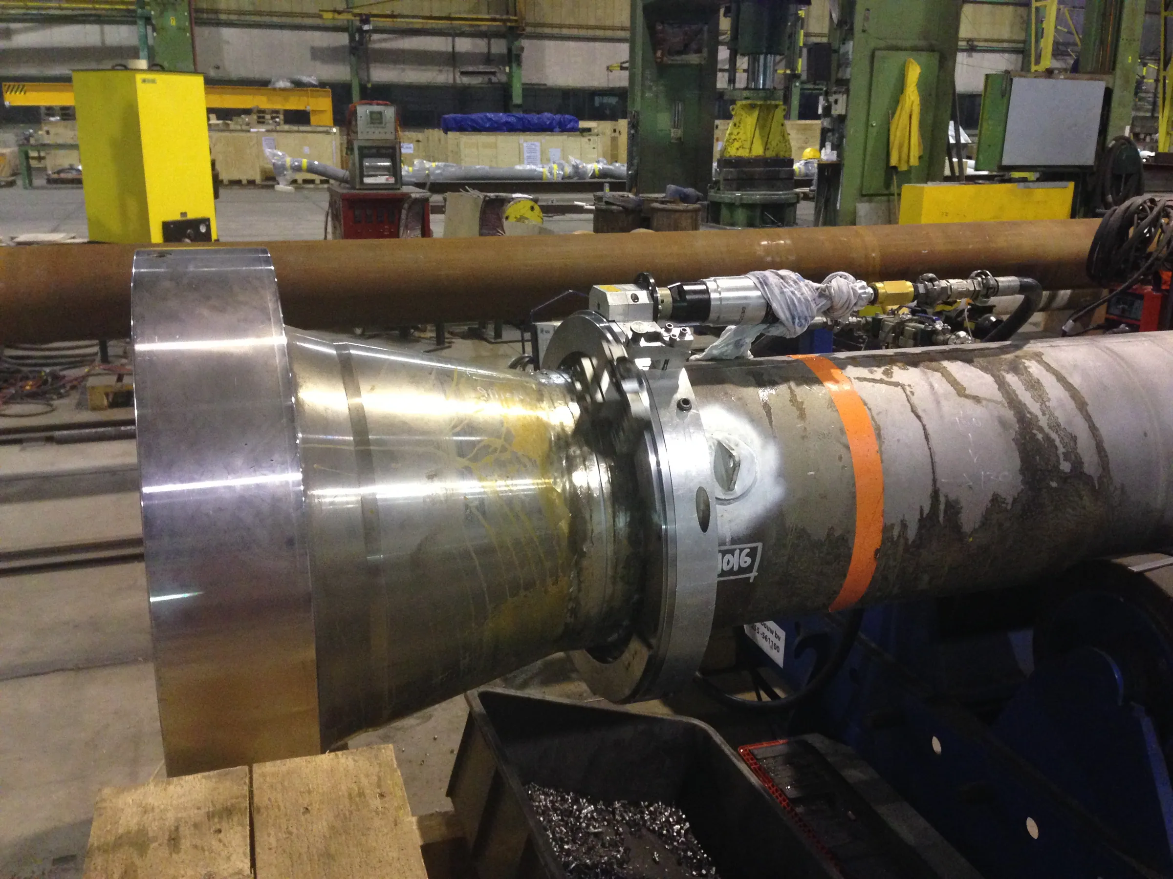 A portable machining head working on a large tapered shaft section in a fabrication hall.