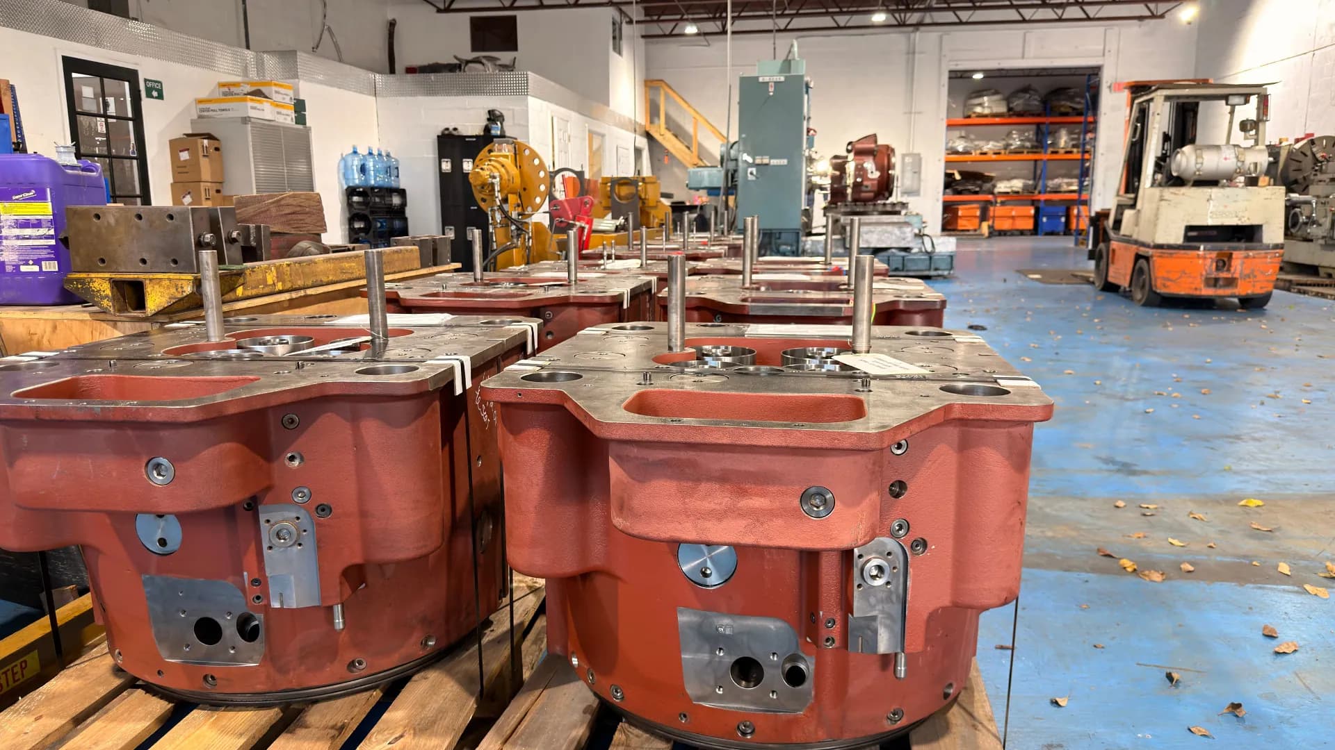 Machined housings on pallets in the OSM workshop, with machine tools and a forklift behind.